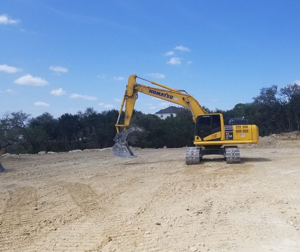 Komatsu excavator working a wide graded pad on a Central Texas site