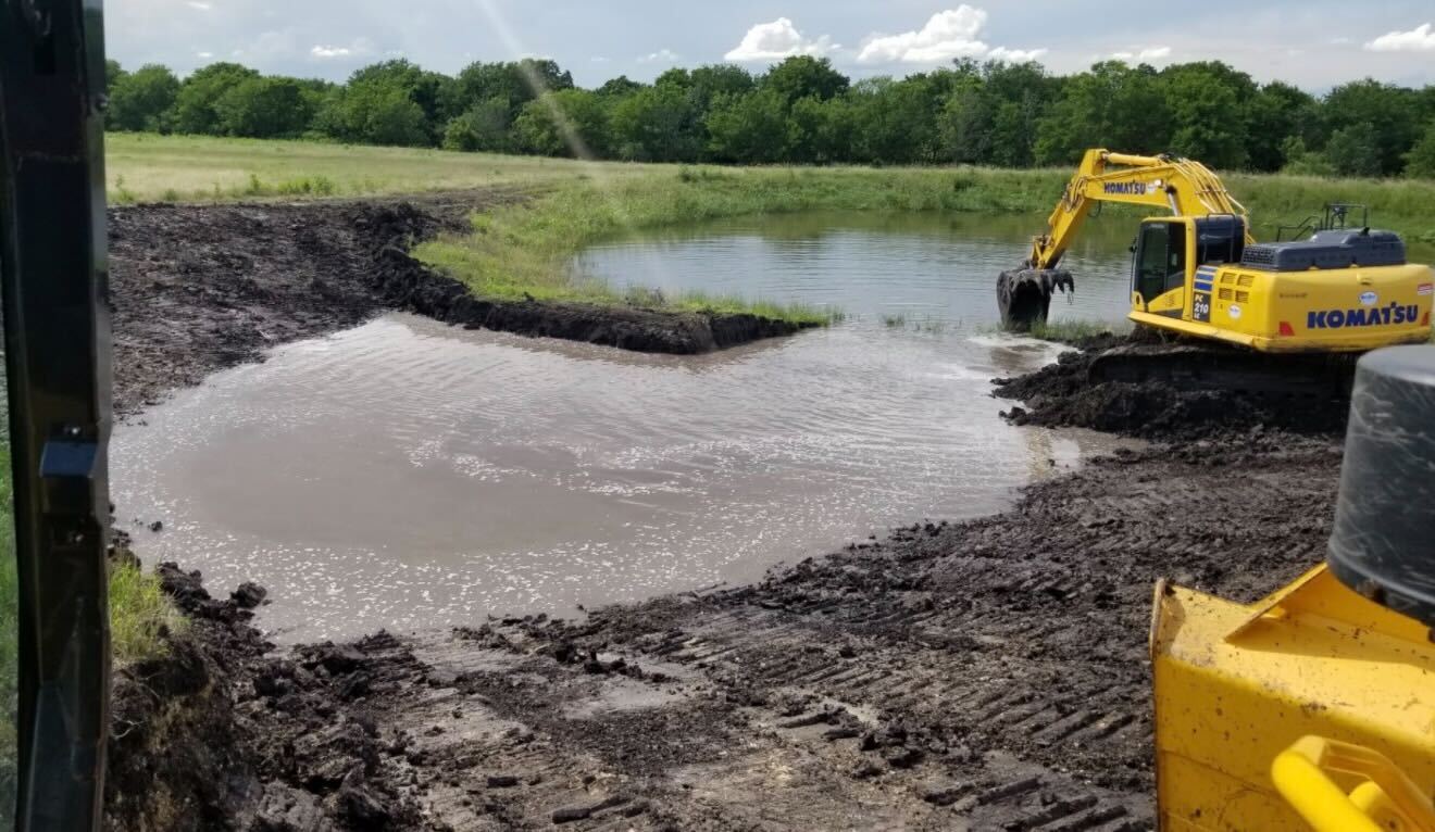 Excavator expanding an existing pond at the water line near Elgin Texas